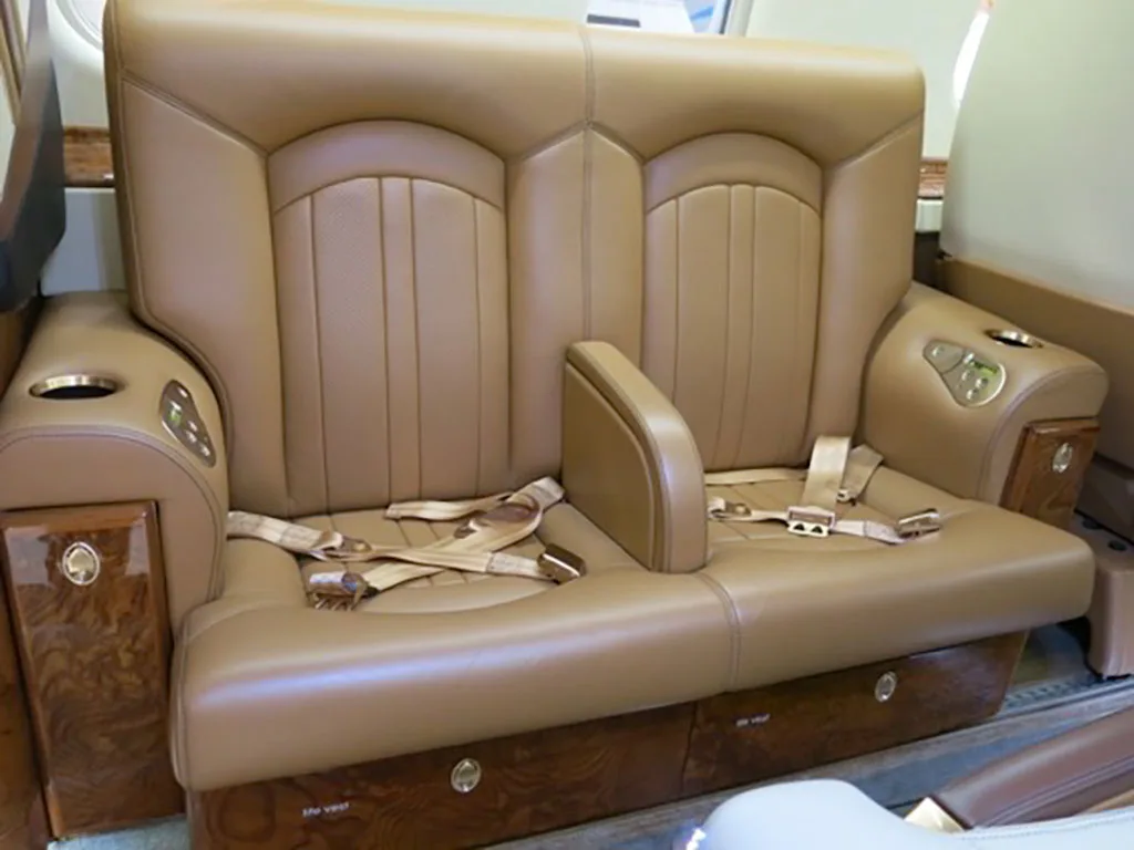 A close-up of a tan leather two-person divan seat with seatbelts in the aircraft cabin.