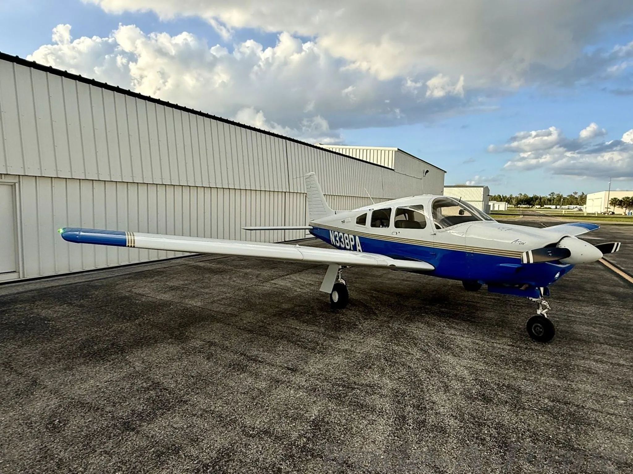 A side view of the white and blue Piper Arrow aircraft (N338PA) parked on the tarmac.