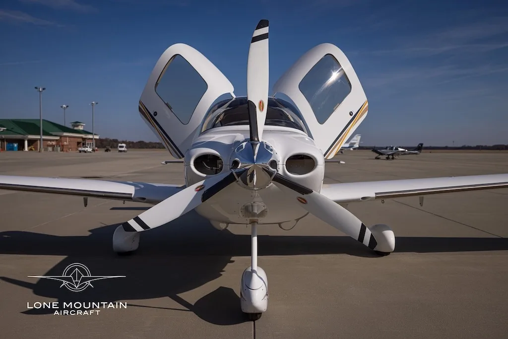 A head-on view of a white Cirrus SR22 aircraft with gold and black stripes, registration N466CE, parked on an airfield with its doors open.