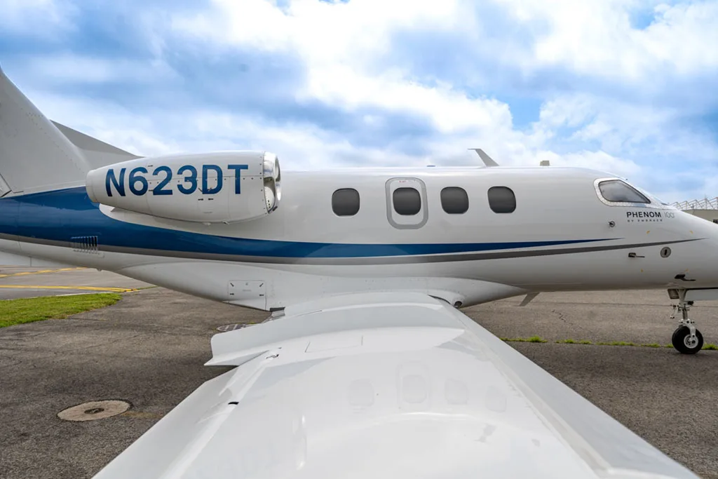 A close-up view of the rear fuselage and wing of a white Embraer Phenom 100, showing the N-number N623DT on the engine nacelle.