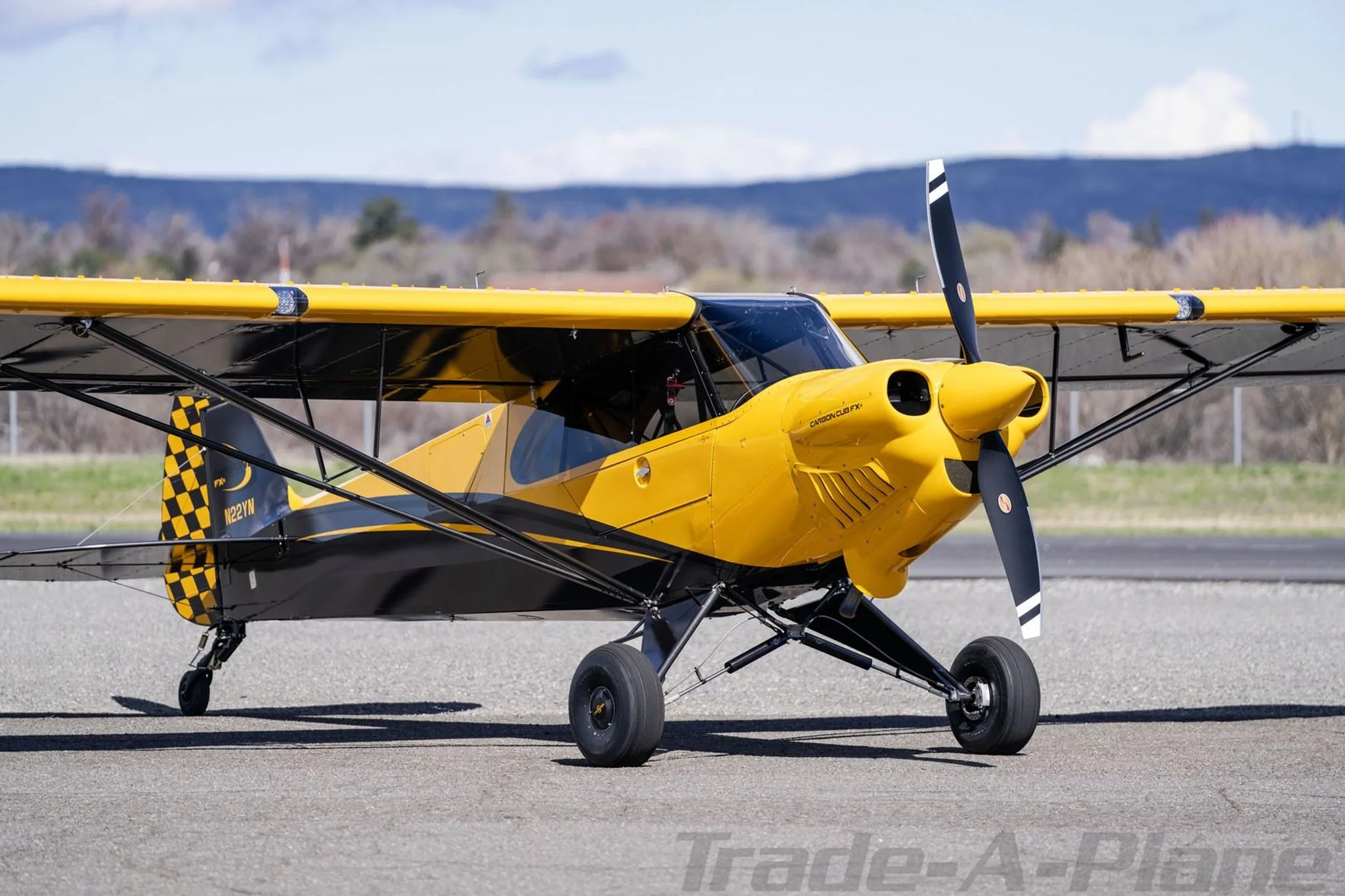 A side view of a yellow and black Carbon Cub FX3 aircraft, registration N22YN, parked on an airfield.