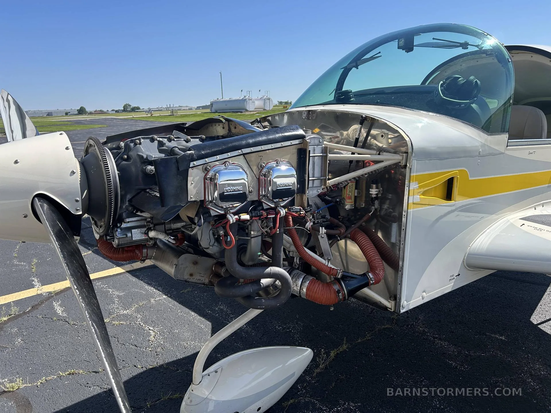 A close-up view of the exposed engine of a white and yellow Grumman AA-5B Tiger aircraft, showing the cylinders and exhaust system.