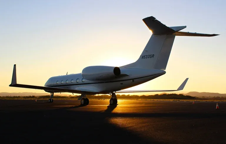 A white business jet, registration N533SR, is parked on an airfield at sunset, viewed from the rear-quarter.