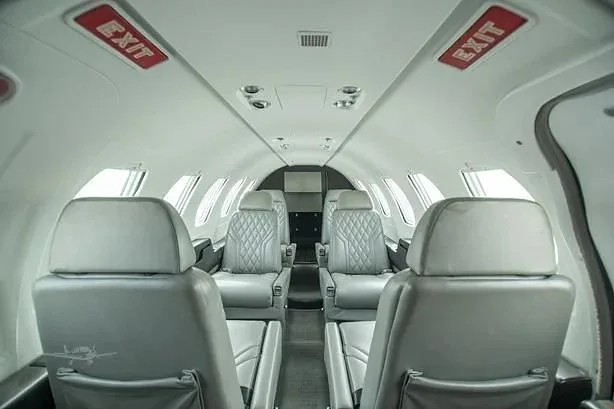 The aircraft's interior cabin features light grey quilted leather seats and red 'EXIT' signs above.