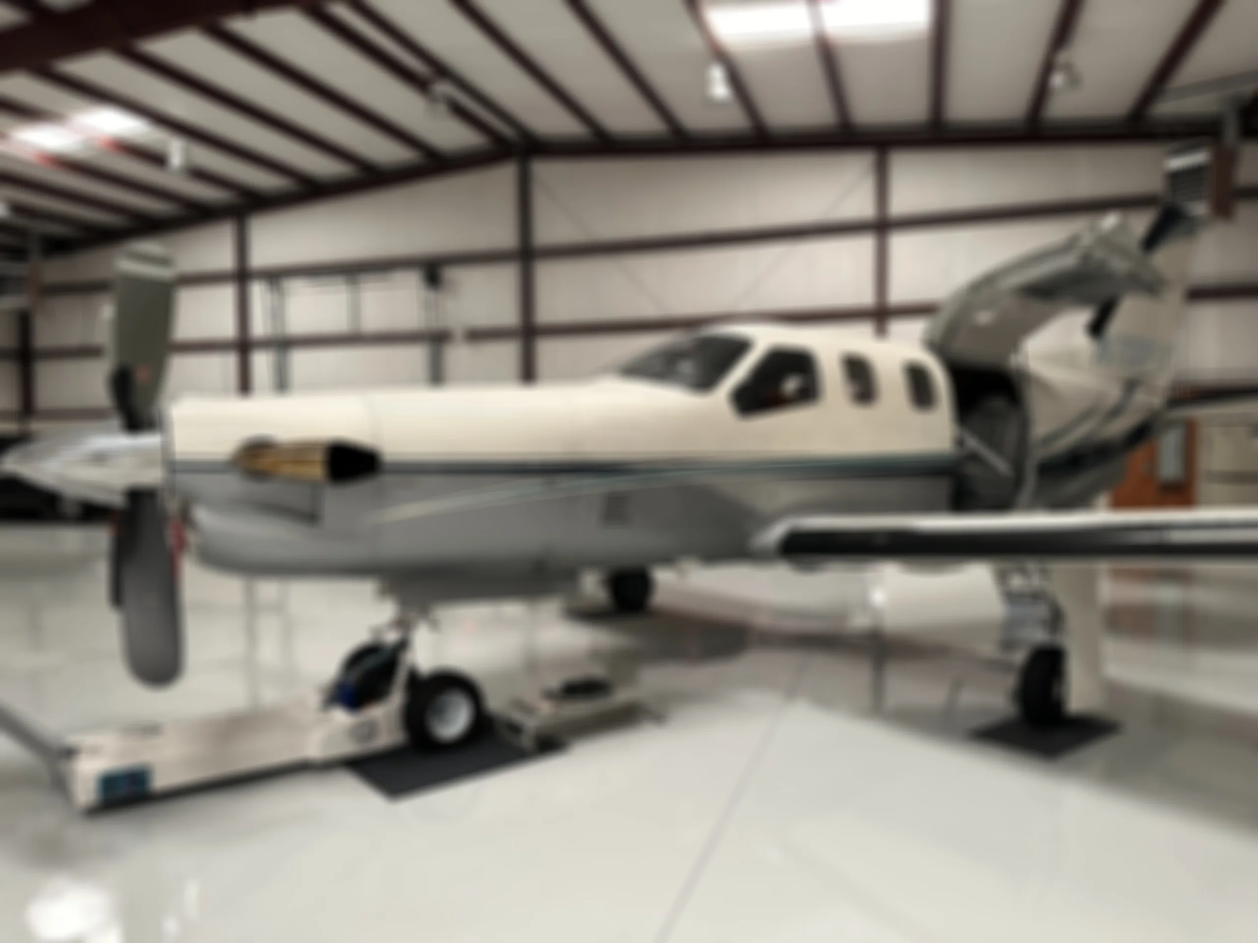 A blurry view of a TBM 940 aircraft with its doors open, parked inside a hangar.