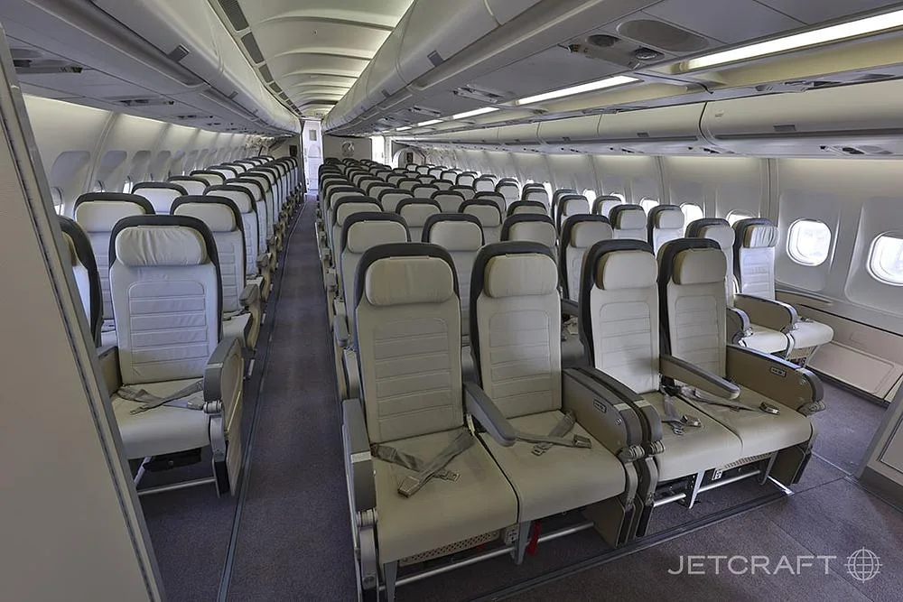 An interior view of an aircraft cabin with rows of light grey economy class seats.
