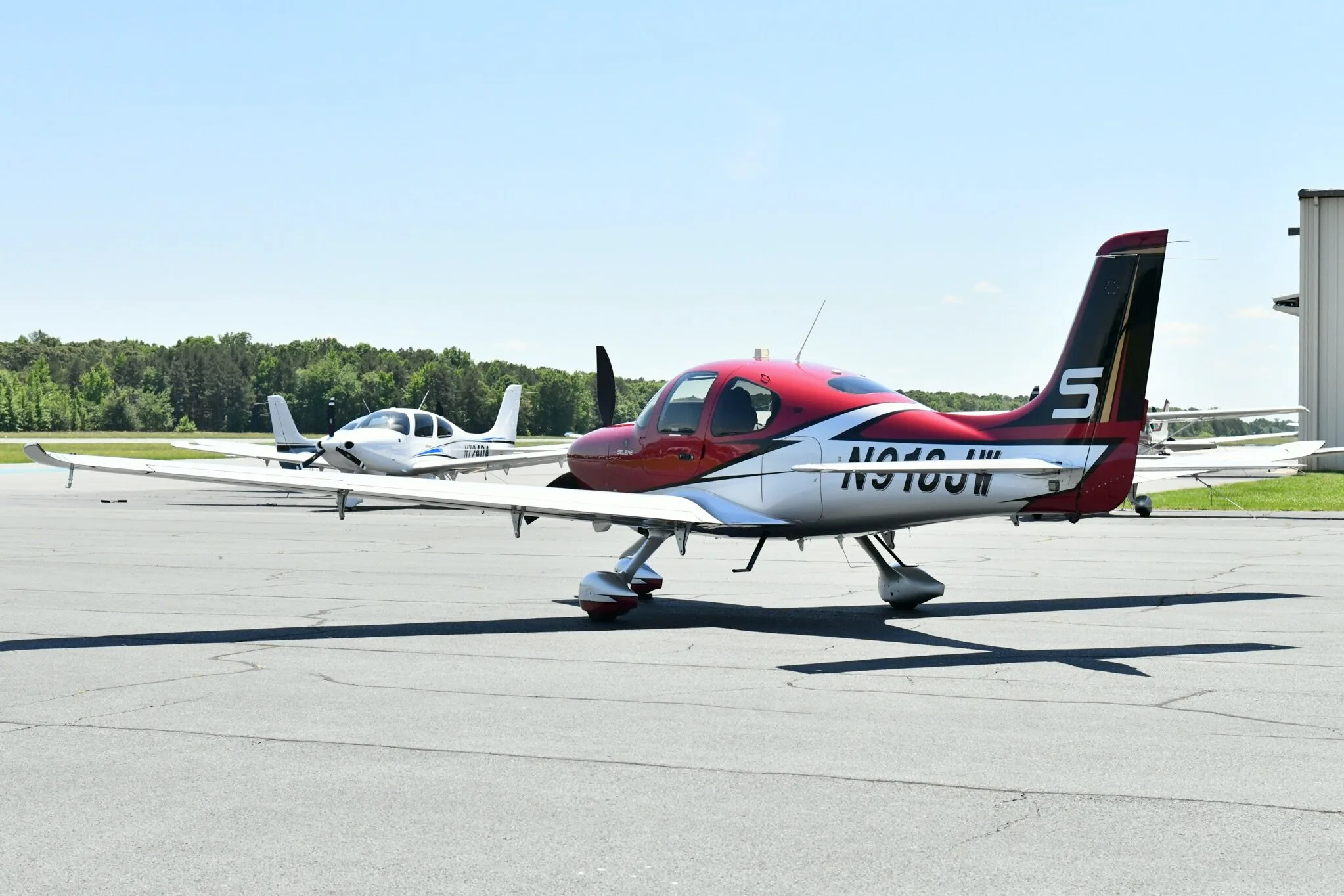 A red and white Cirrus SR22T aircraft with registration N918JW parked on an airfield with another white aircraft in the background.