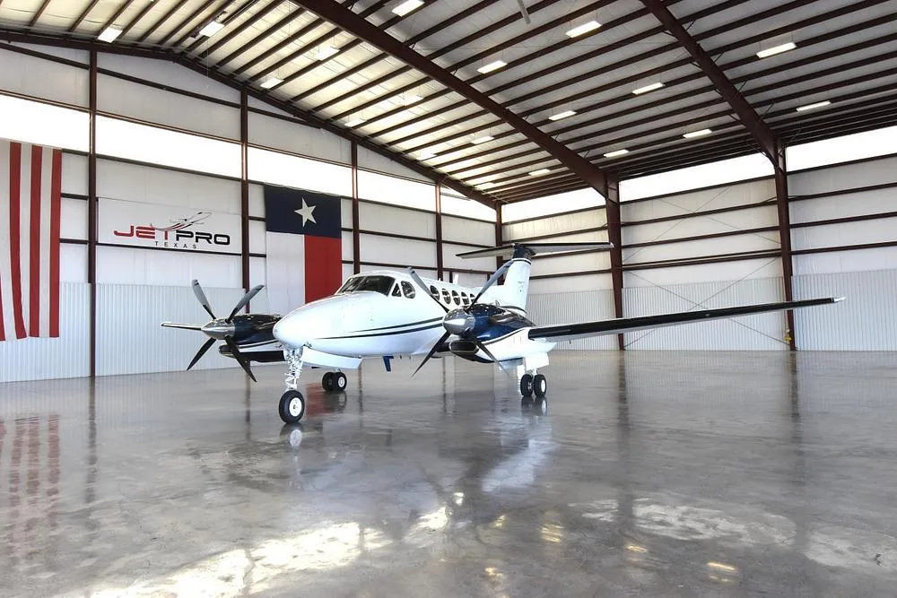 A front-left view of the white and blue Beechcraft King Air twin-engine turboprop aircraft, N627MG, in a hangar.