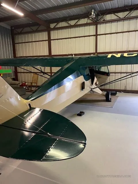 The tail section of a beige and dark green aircraft parked inside a hangar.