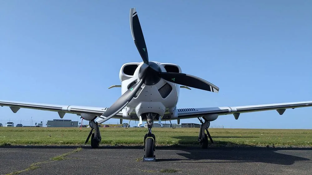 A white propeller aircraft with a black propeller, viewed head-on on an airfield.