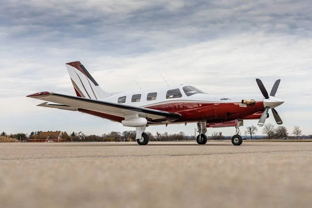 A white and maroon single-engine turboprop aircraft viewed from the front-right, parked on an airfield.