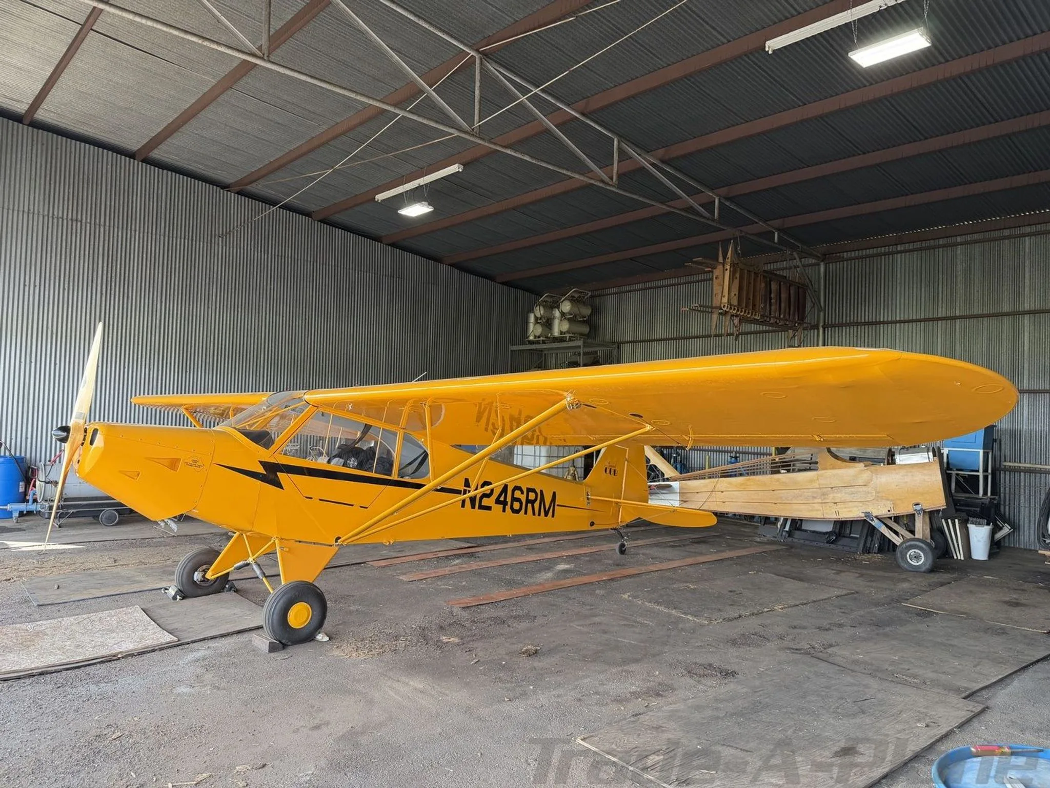 Side view of a yellow American Legend Cub aircraft with registration N246RM in a hangar.