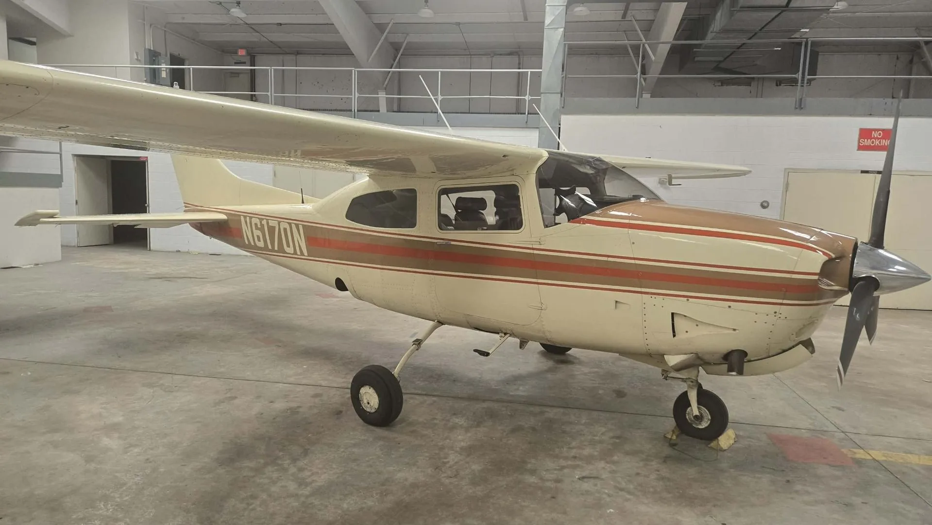 A side view of the N6170N aircraft, a white and brown high-wing single-engine plane, parked inside a hangar.