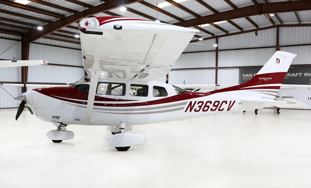 A white and red Cessna Stationair TC aircraft (N369CV) is parked in a hangar, viewed from the rear left.