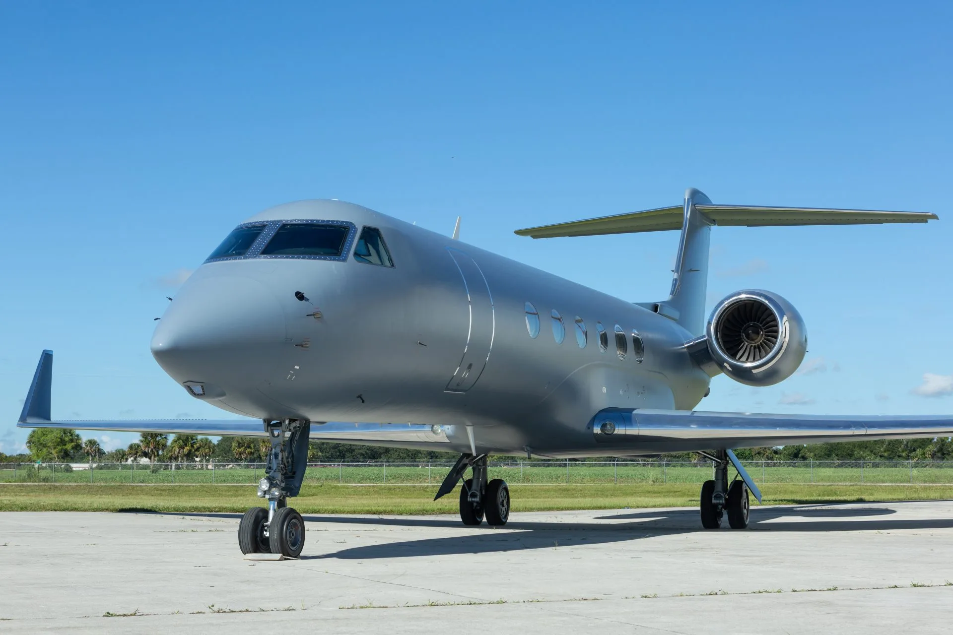 A sleek grey business jet, likely a Gulfstream, is parked on an airfield under a clear blue sky.