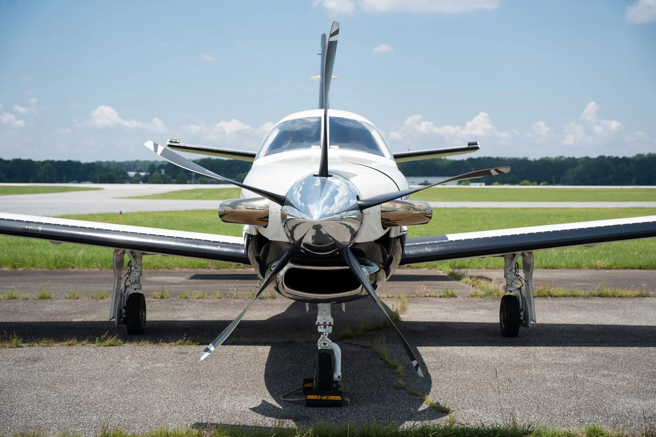 A head-on view of a white and black TBM 960 aircraft with its propeller blades visible, parked on an airport tarmac.