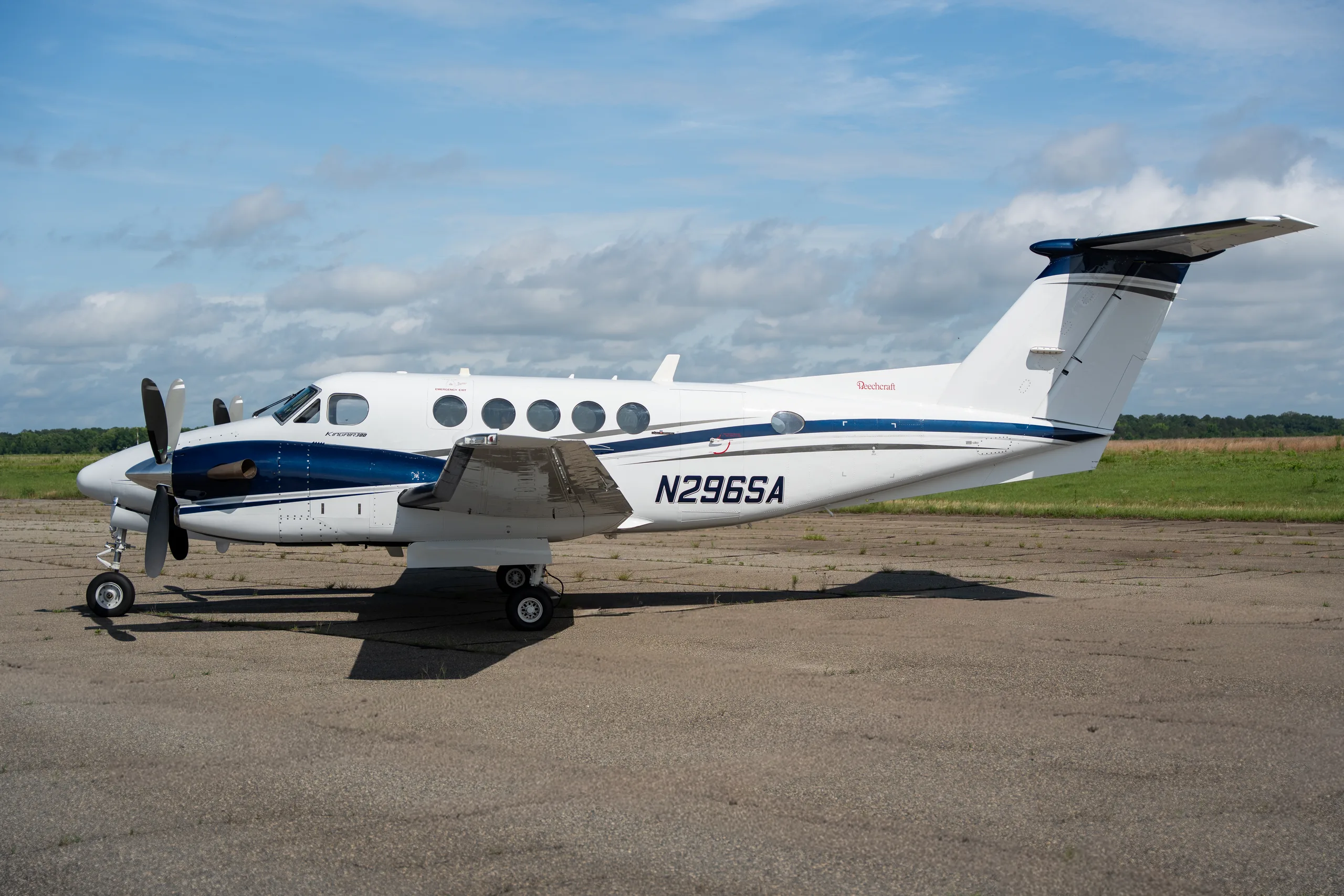 A side view of the N296SA Beechcraft King Air twin-turboprop aircraft with a white and blue paint scheme on a tarmac.