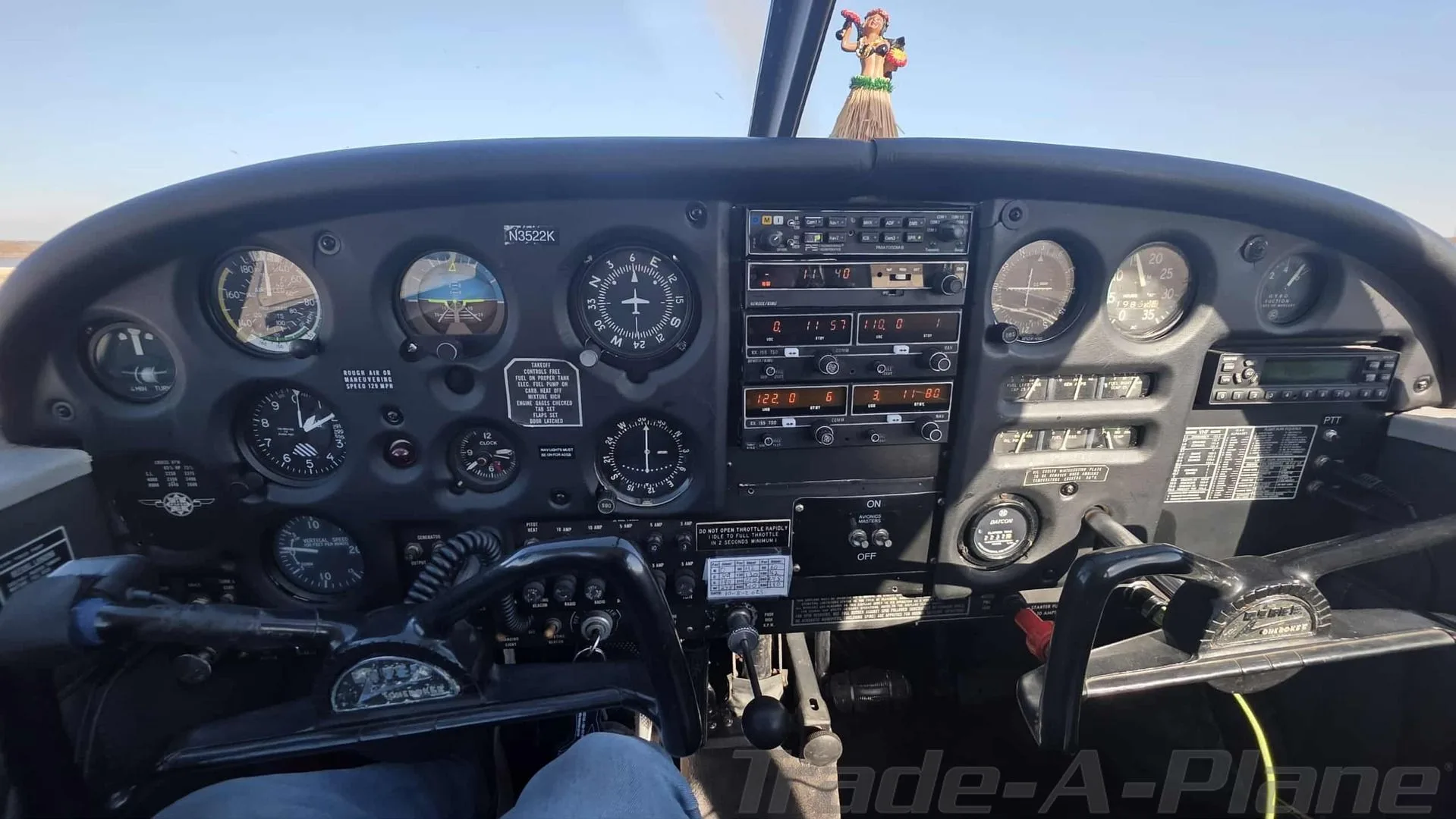 The instrument panel of the aircraft, showing gauges, radios, and controls, with a hula doll on the glare shield.