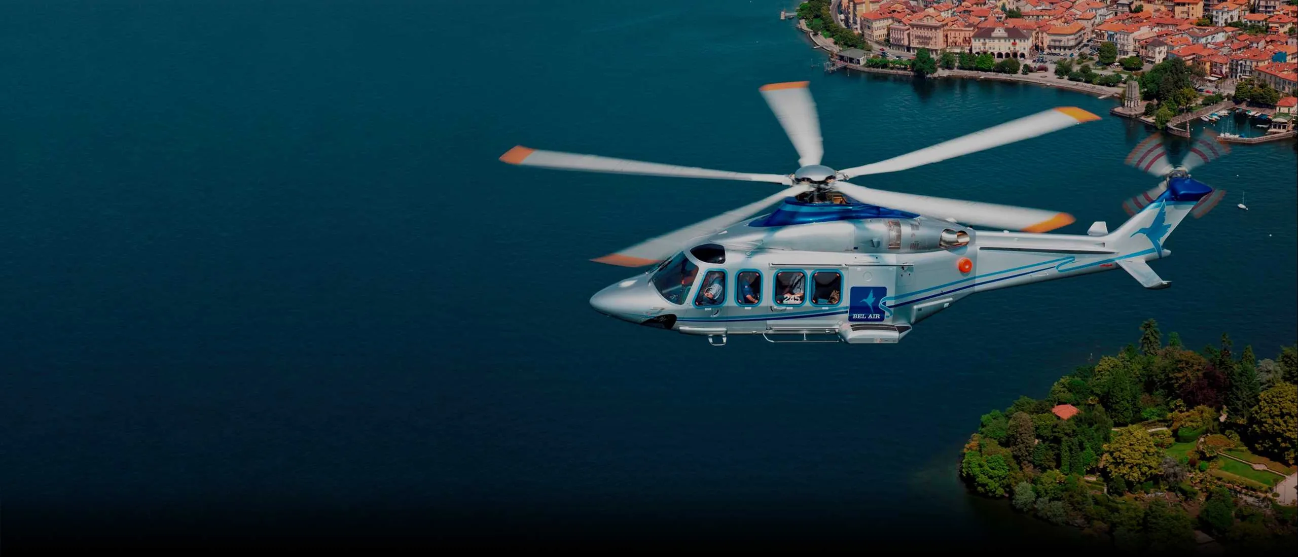 AgustaWestland AW139 helicopter flying over a lake near a town.