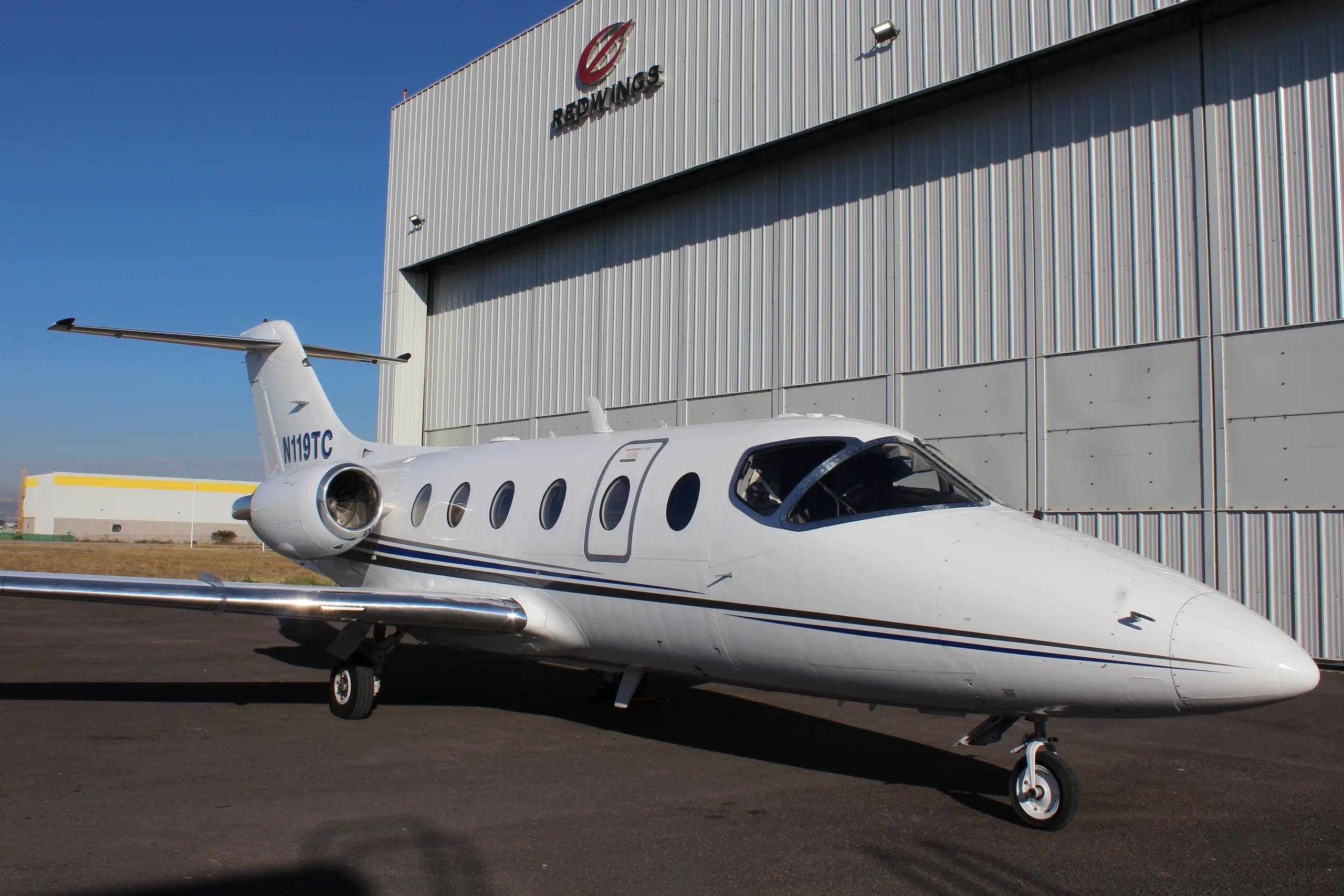 A Learjet 25D with registration N119TC parked in front of a hangar.