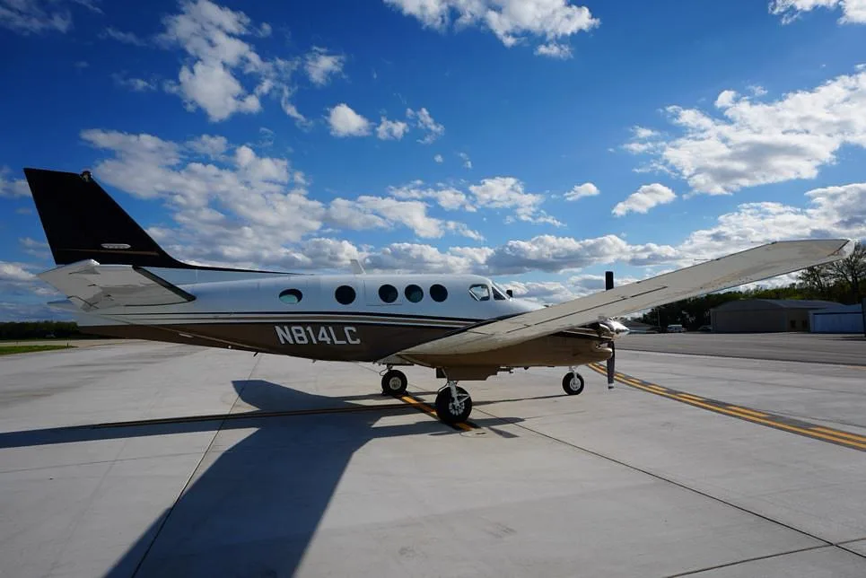 A side view of the Beechcraft King Air 200, registration N814LC, parked on an airfield under a partly cloudy sky.