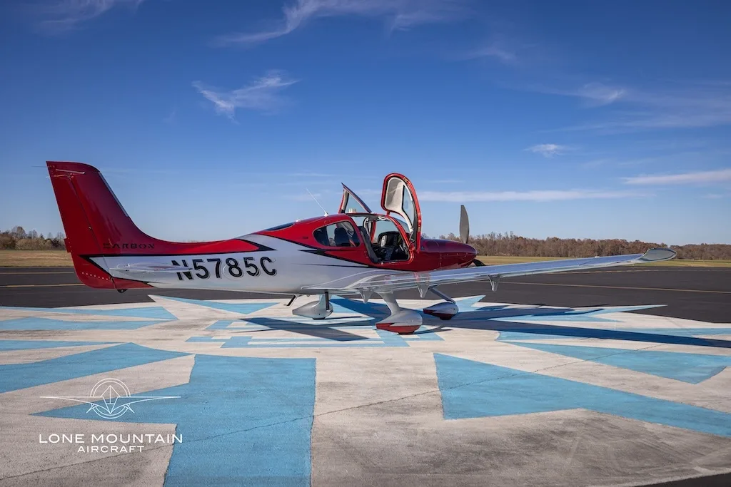 A side view of a red and white Cirrus SR22 aircraft with registration N5785C parked on an airfield with its doors open.