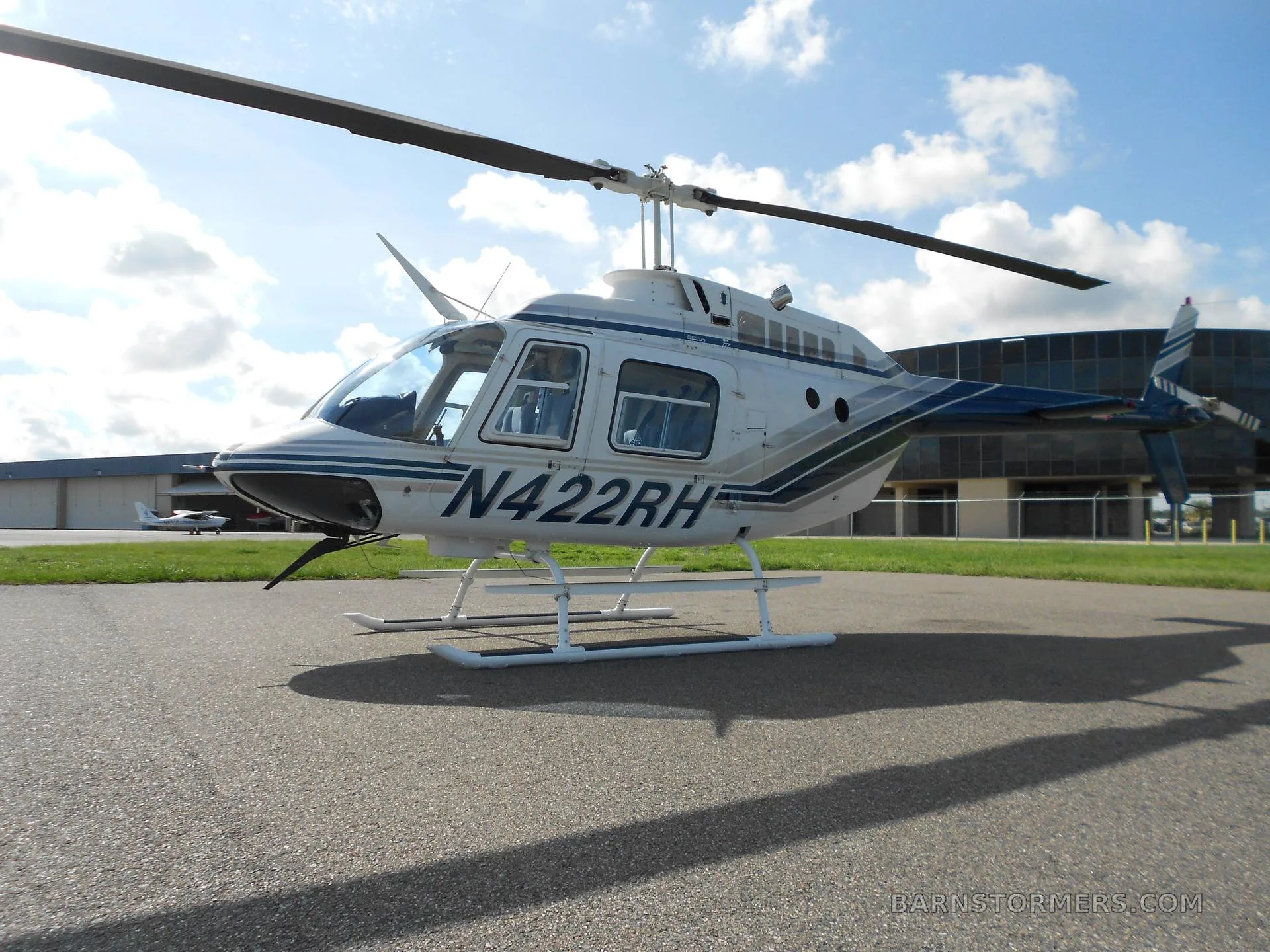 A white and blue Bell 206 helicopter (N422RH) parked on an asphalt apron with the sun behind it.