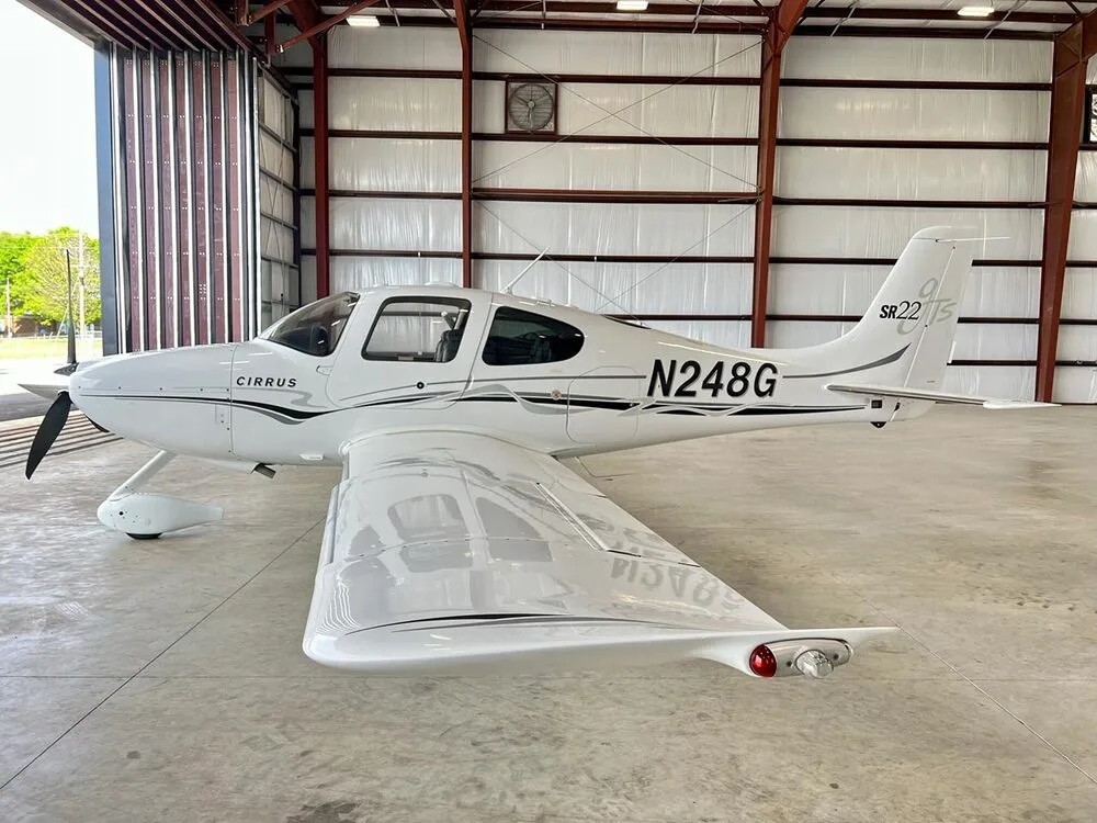 A white Cirrus SR22 aircraft with black and grey stripes, registration N248G, parked in a hangar.