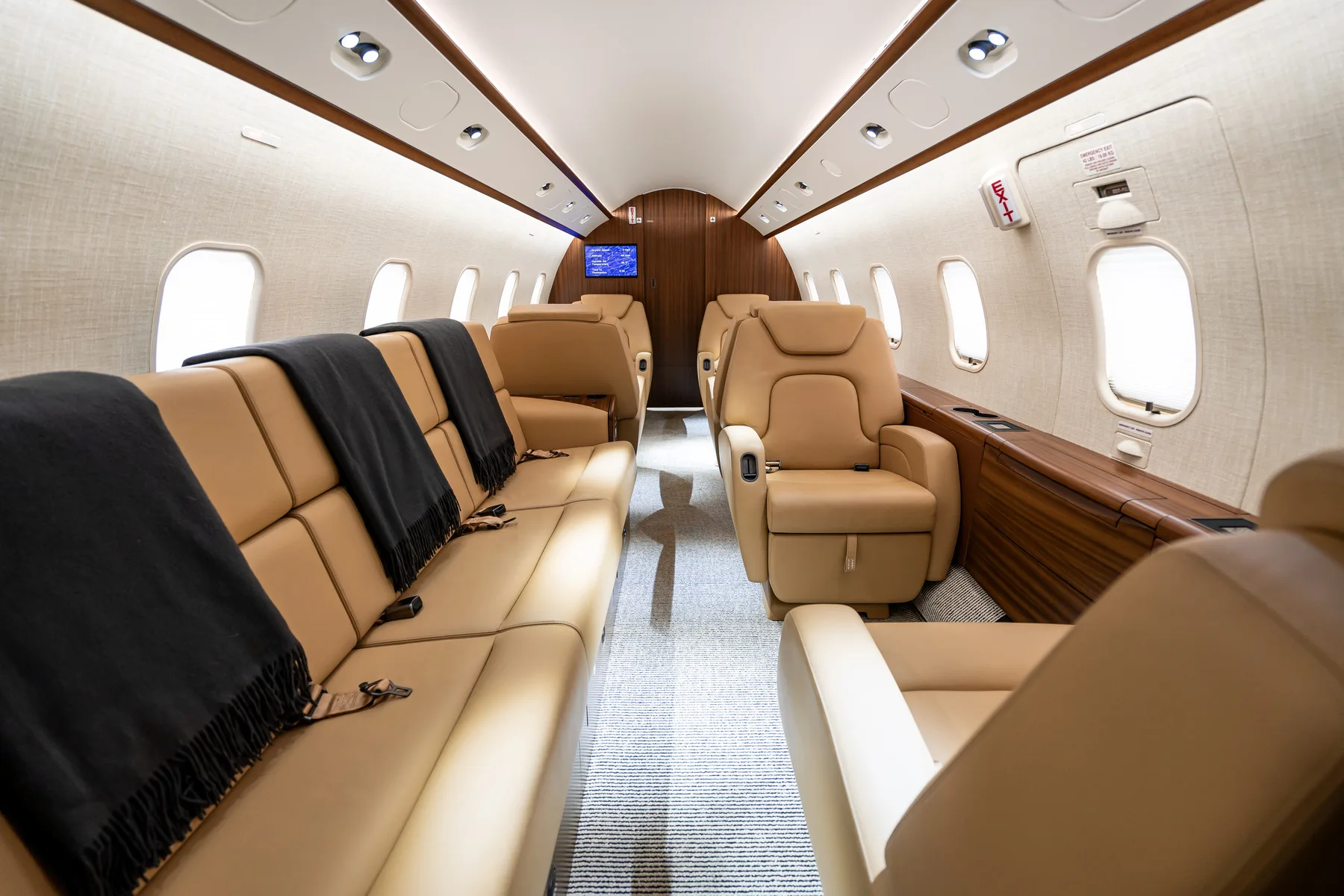 A luxurious private jet interior with tan leather seats and dark blankets.