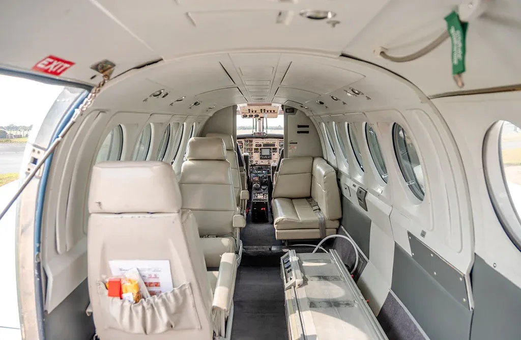 The interior cabin of a private aircraft with beige leather seats, an exit door, and a view towards the cockpit.