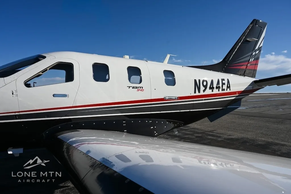 A close-up view of the rear fuselage and wing of a TBM 940 aircraft, registration N944EA, showing its white, black, and red paint scheme.
