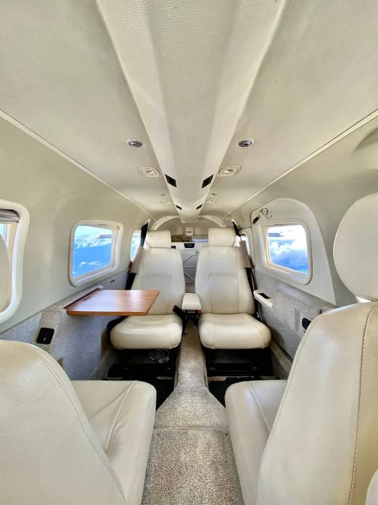 The cream-colored interior cabin of a small aircraft, showing four passenger seats and a small table.
