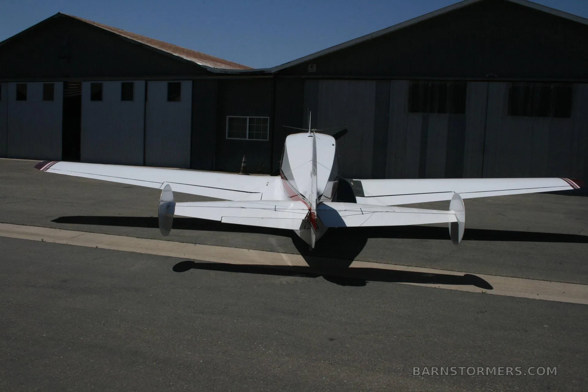 Rear view of a white and maroon single-engine aircraft, tail number N8352R, parked on an asphalt apron in front of hangars.