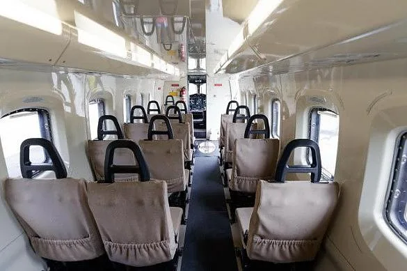 A view down the aisle of an aircraft cabin, showing multiple rows of beige passenger seats.