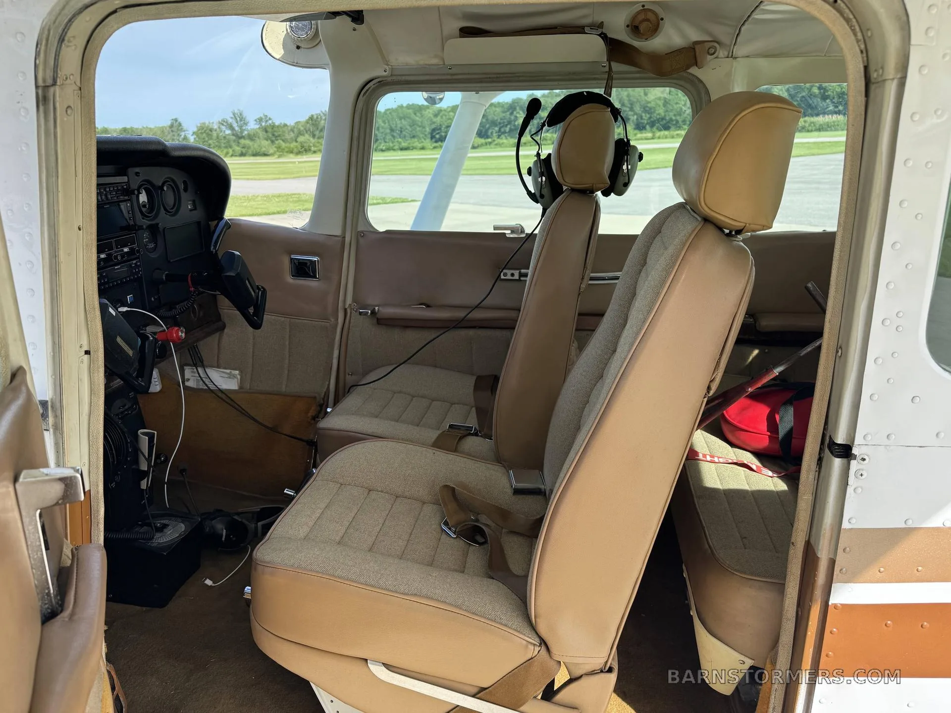 The interior cabin of a Cessna aircraft shows tan seats and a partial view of the instrument panel.