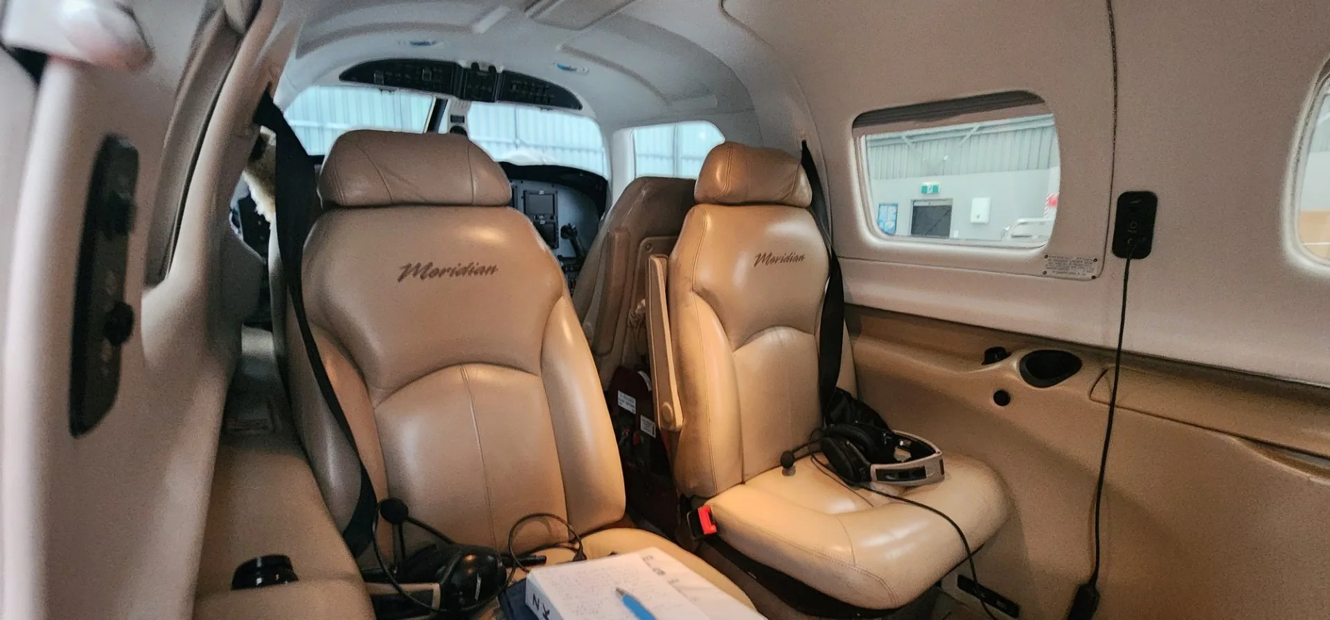 The tan leather passenger seats of an aircraft cabin, with "Meridian" embroidered on the headrests, looking towards the cockpit.