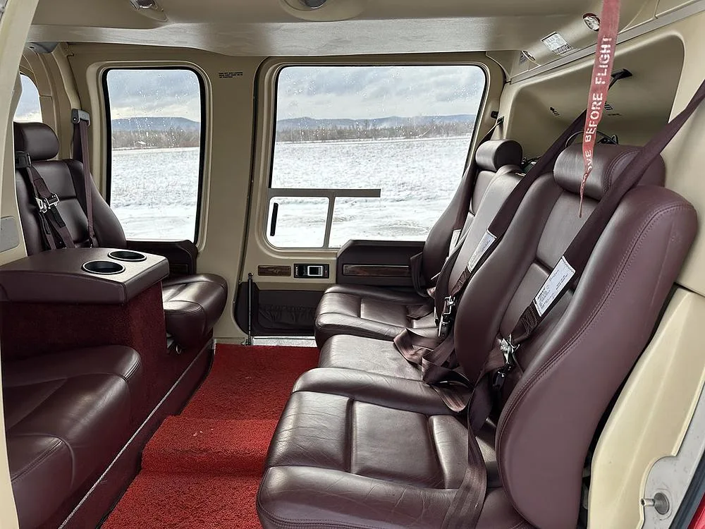 The interior of a helicopter cabin featuring brown leather seats, a red carpet, and large windows overlooking a snowy landscape.