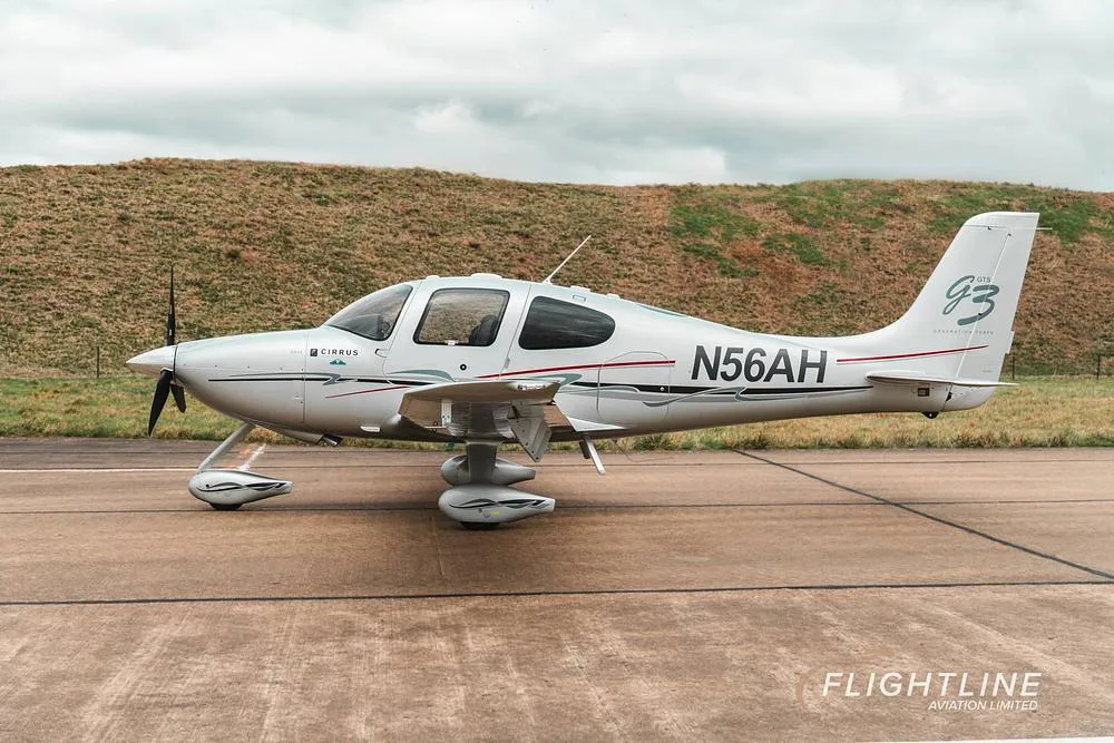 A side profile view of the white Cirrus SR22 aircraft N56AH with red and gray accents on a tarmac.