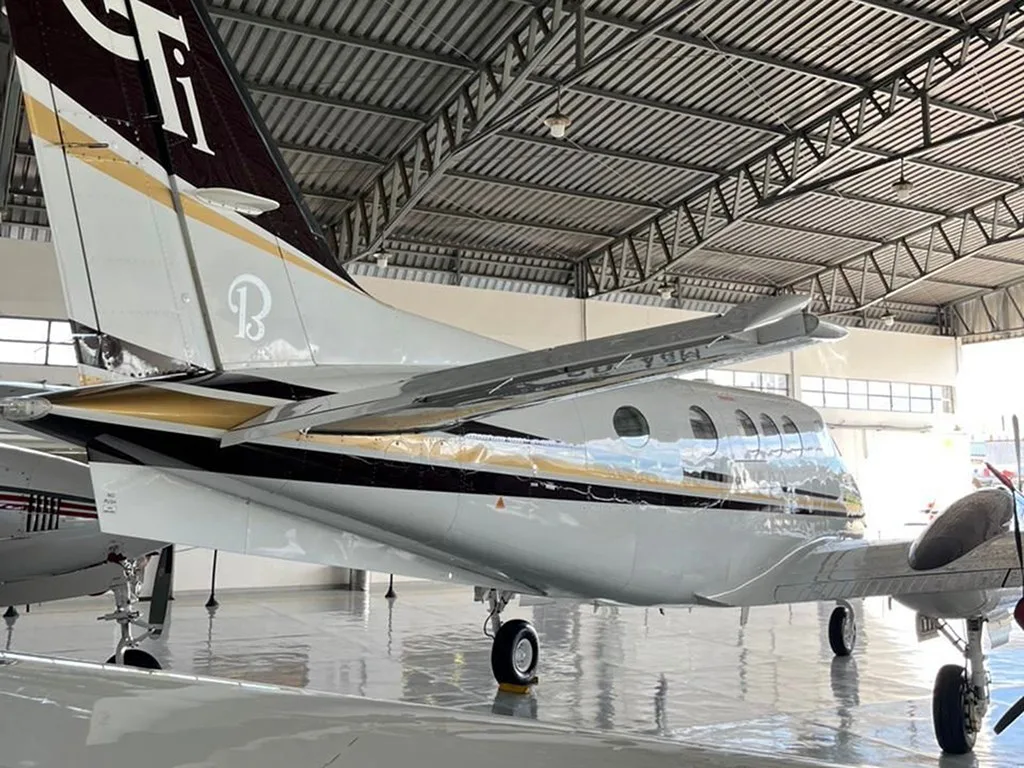 Rear-side view of a white and gold Beechcraft King Air 350 with a 'GT' tail logo, parked inside a hangar.