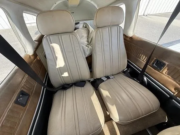 The light brown leather rear seats of a small aircraft cabin, with seatbelts visible.