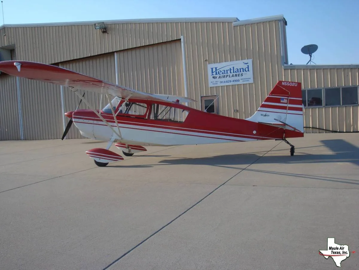 A red and white Bellanca aircraft, registration N5502U, is parked on an airfield tarmac in front of a hangar.