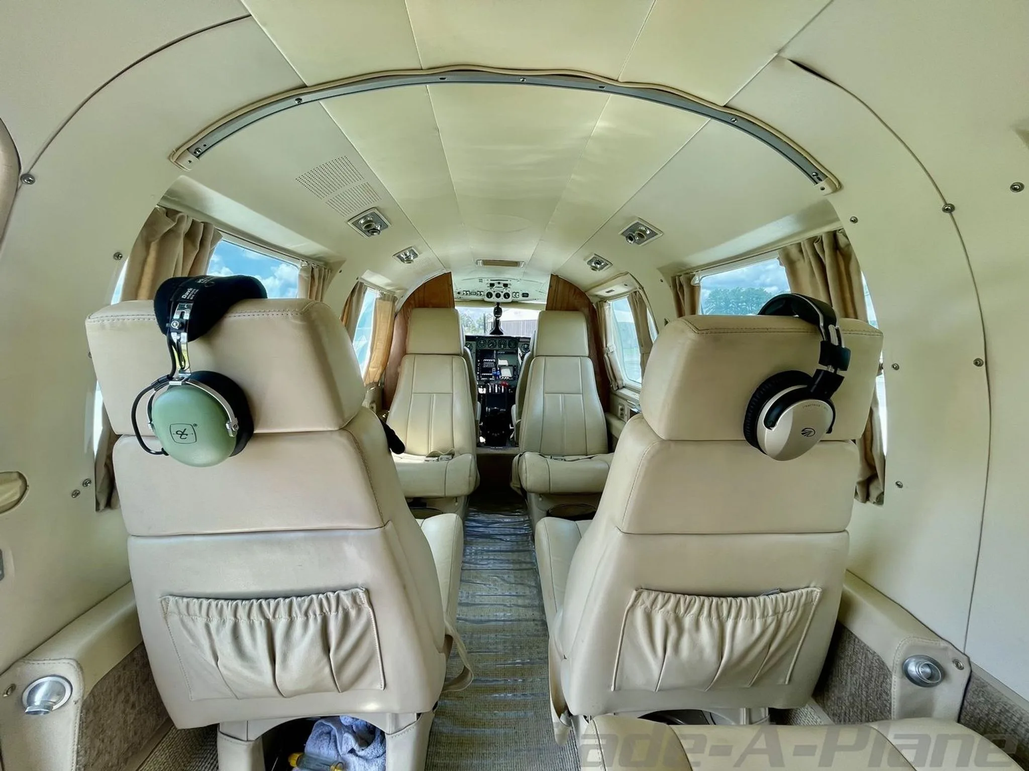 The beige leather interior cabin of the aircraft, viewed from the rear, showing multiple passenger seats and headphones.