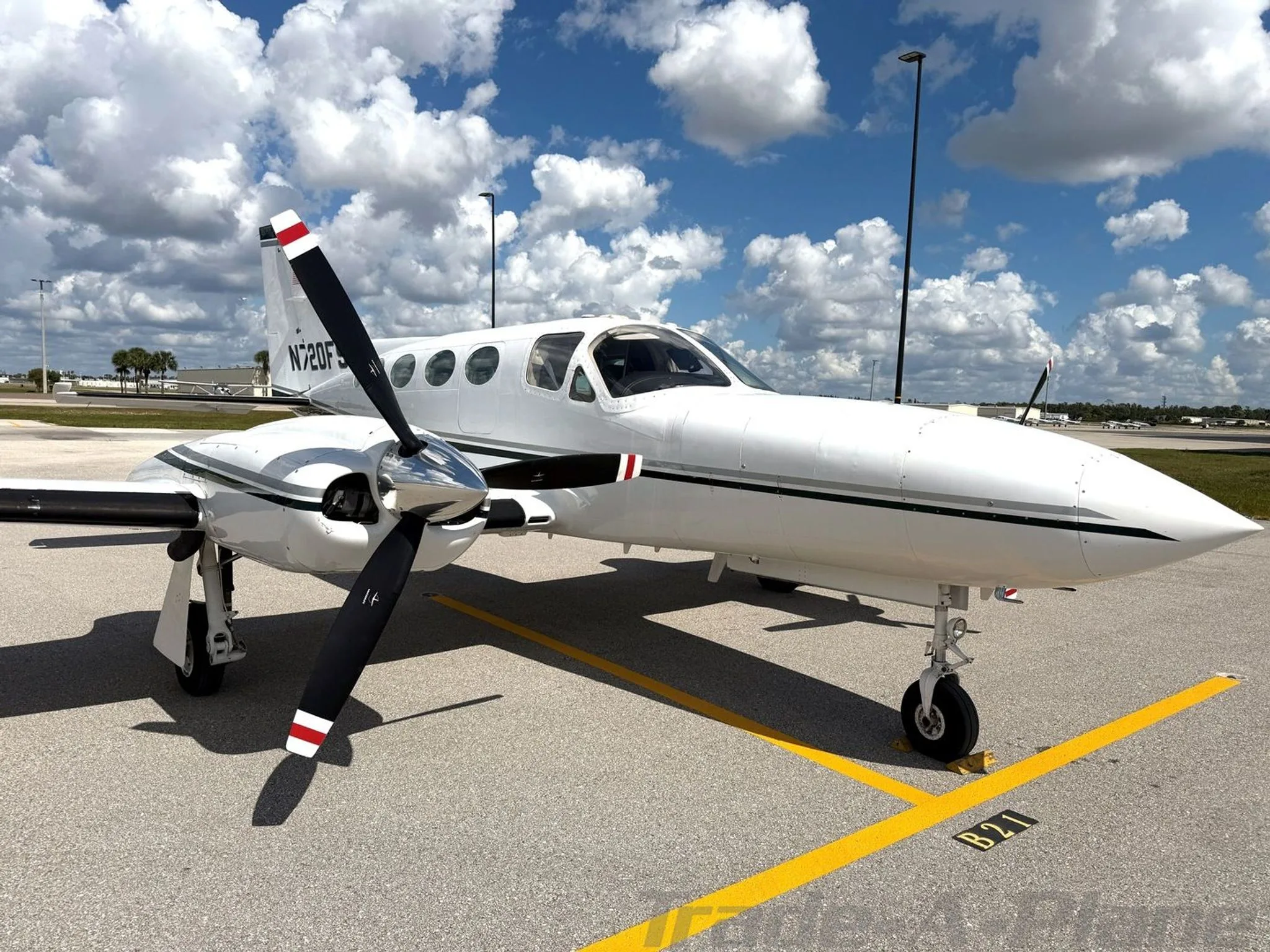 A white Cessna 414 Chancellor aircraft, N720FS, with dark green stripes, parked on an airfield, viewed from the front right showing the nose and right engine.