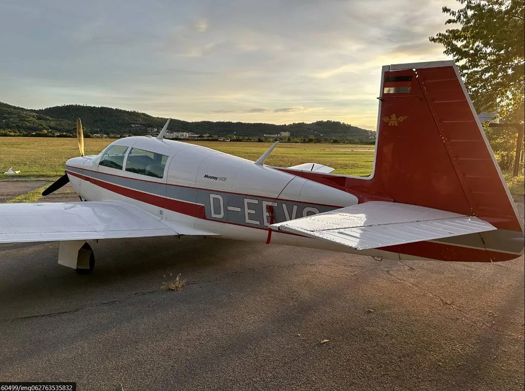 A white and red Mooney M20J aircraft (D-EEVO) seen from the rear-right, parked on an tarmac at sunset.