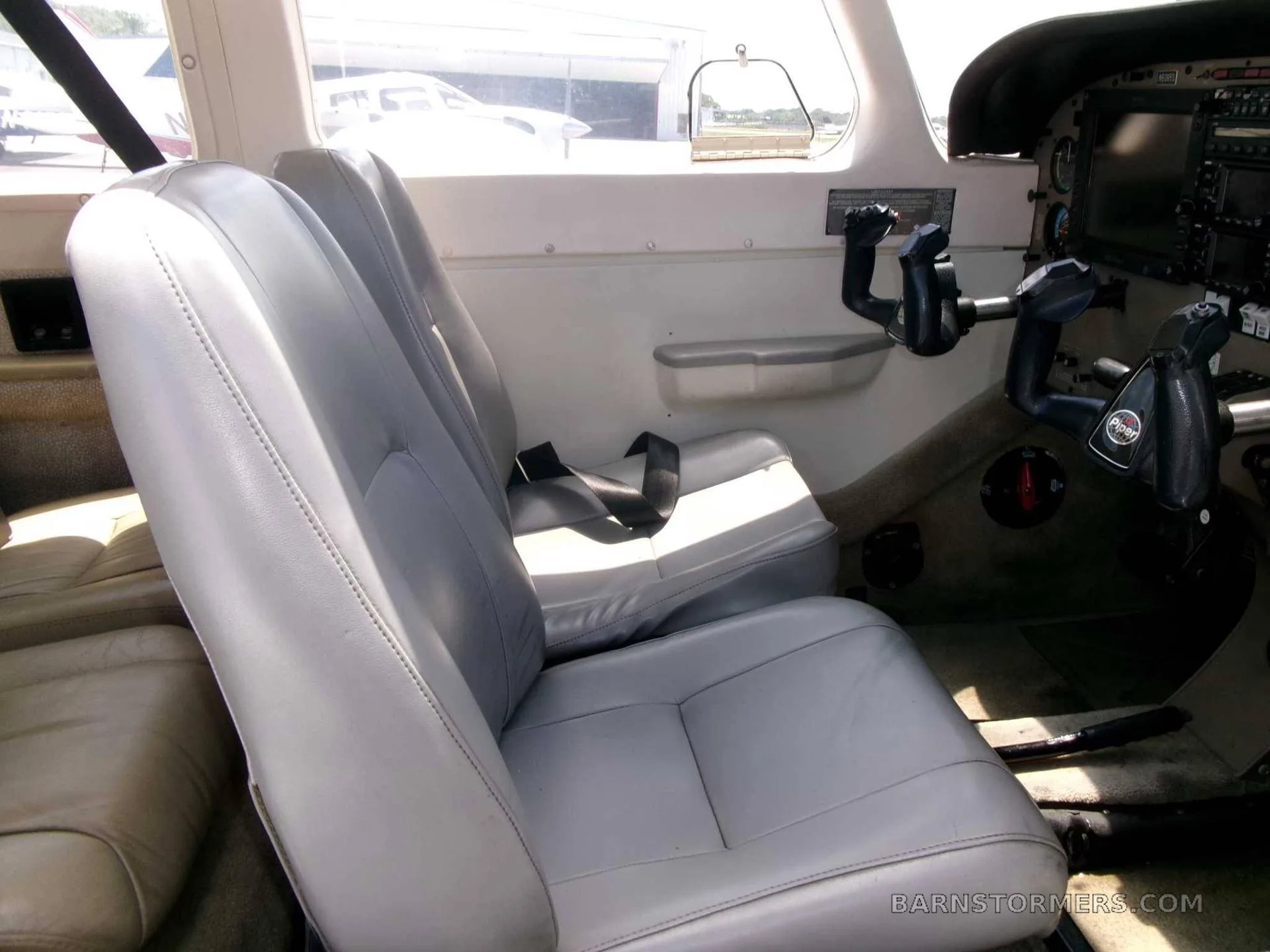 The light gray leather interior seats of a small aircraft, with the cockpit visible in the background.