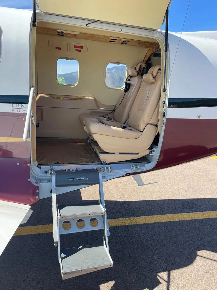 An aircraft's open passenger door with integrated stairs leading into the tan leather cabin.