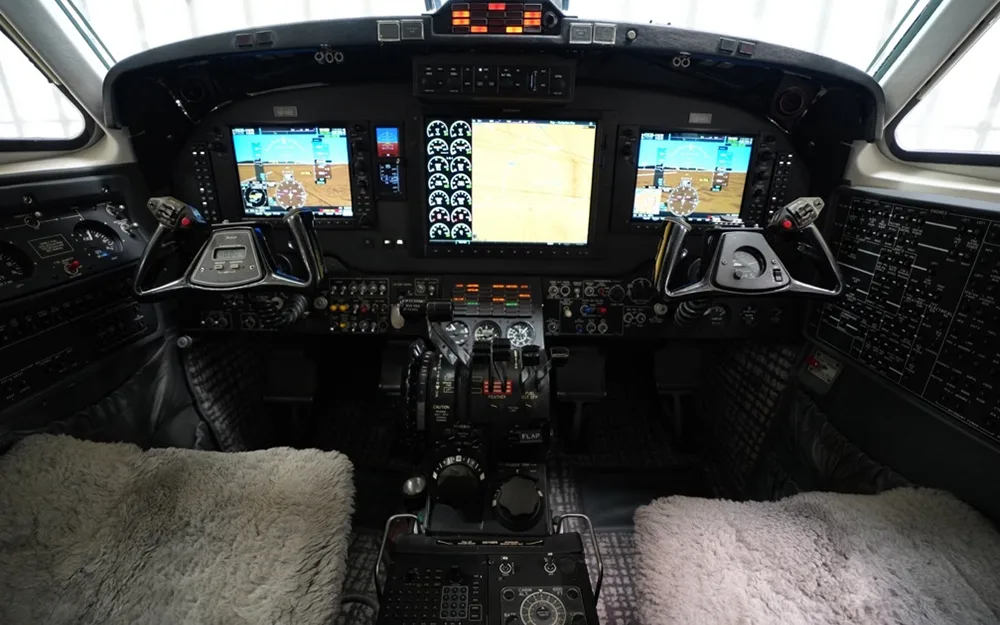 The modern glass cockpit of a turboprop aircraft, featuring multiple digital displays and control yokes.