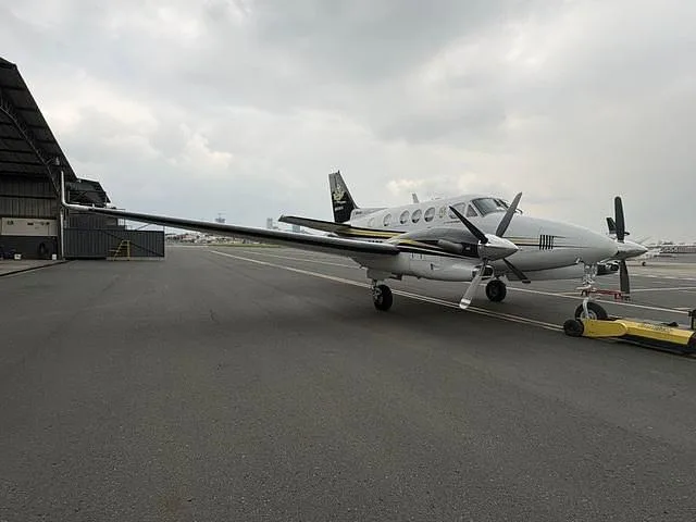 A white and black twin-engine turboprop aircraft with yellow stripes parked on an airfield, viewed from the front-right.
