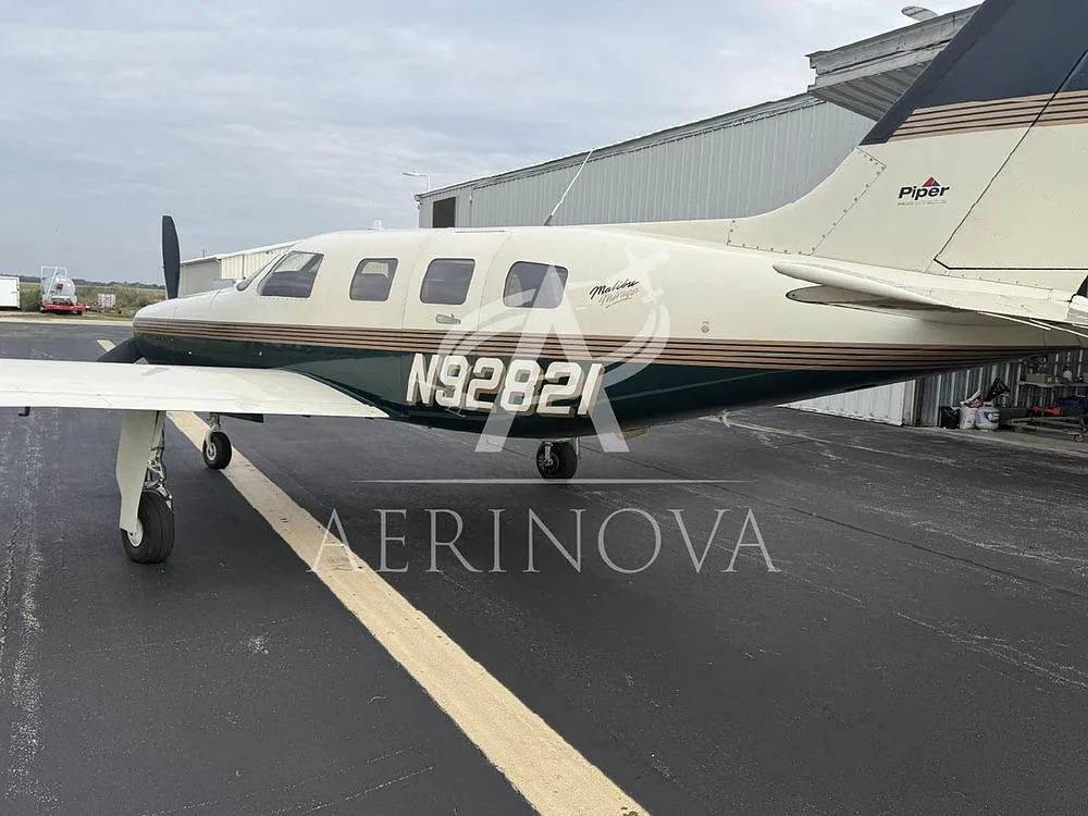 A side view of the Piper Malibu Mirage N92821 in dark green and cream, parked near a hangar.