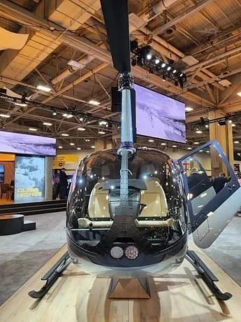 A black helicopter with a clear bubble canopy and tan interior seats, displayed indoors with one door open.